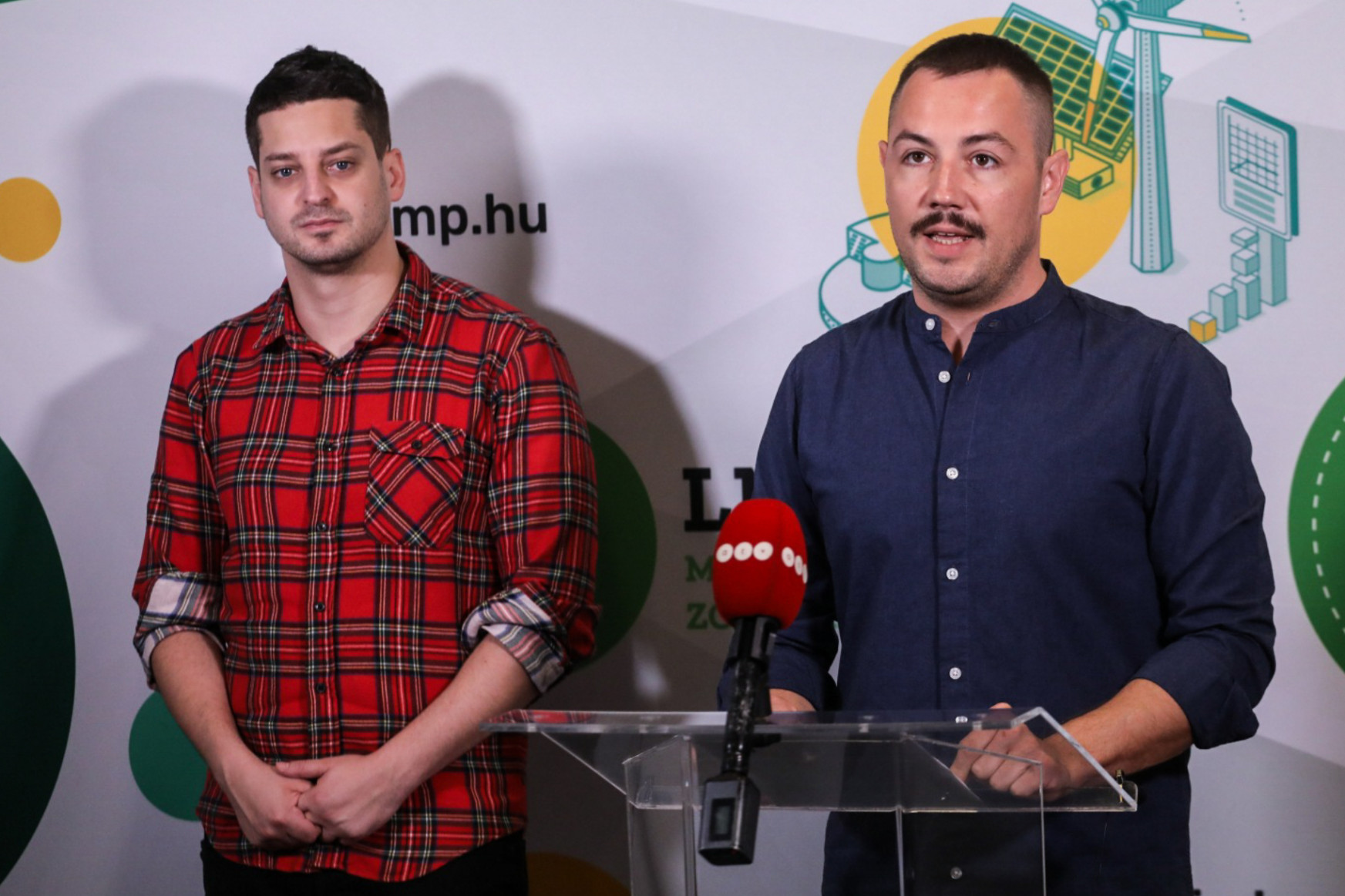 Két meleg politikus kezében trappista sajttal egy akkugyár előtt
